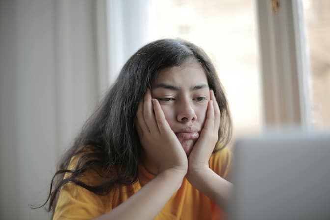 Person looking melancholic while watching laptop at home, representing lack of motivation